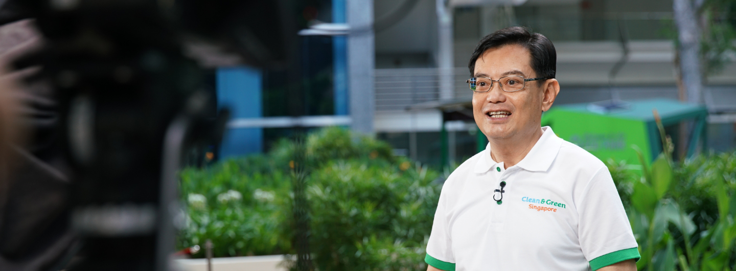 Man in Clean & Green Singapore polo shirt stands before camera, outdoor setting.